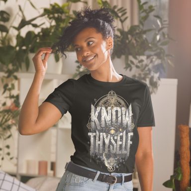 Smiling woman in a black t-shirt with the phrase "Know Thyself" and a decorative design.